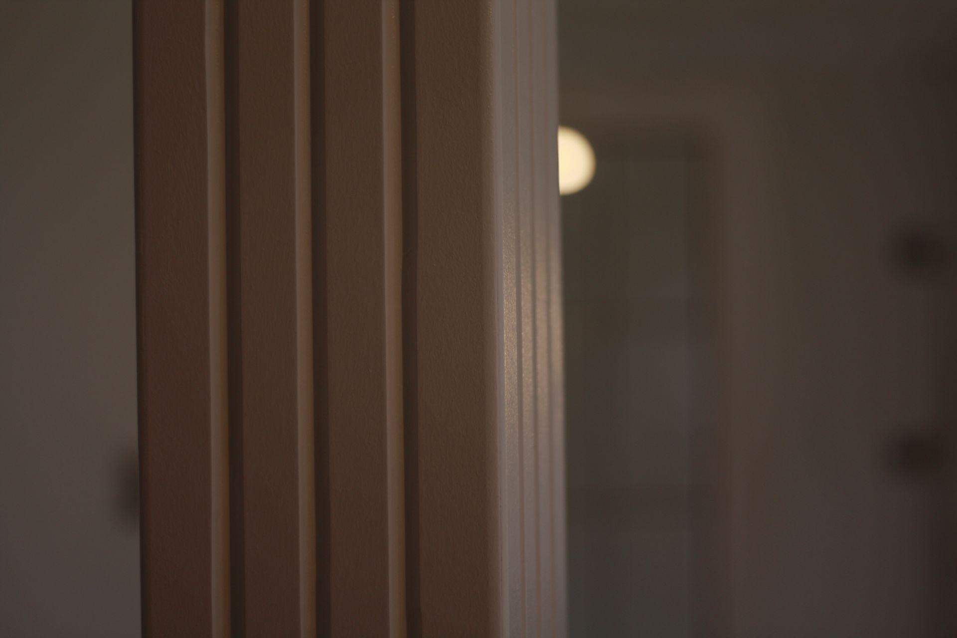 Close-up view of an interior wooden column with vertical grooves and a blurred background.