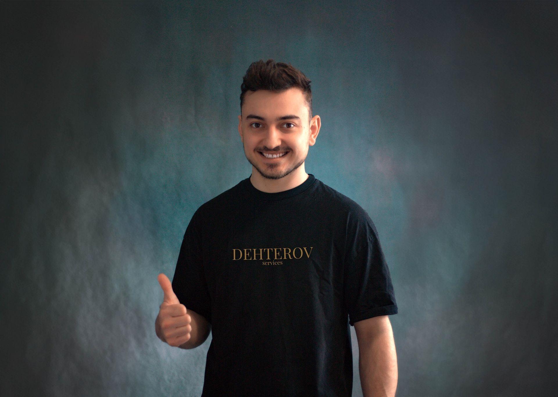 Smiling person in a black t-shirt giving a thumbs up against a dark green background.